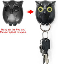 Black owl-shaped key holder with a key attached, showing how it opens its eyes when a key is hung on it.