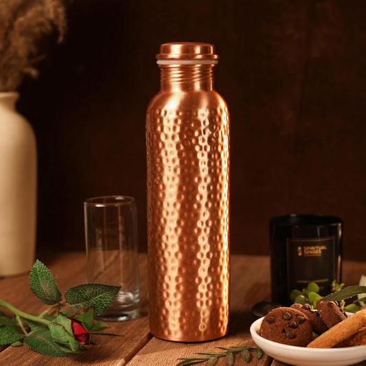 Copper water bottle on a wooden table with cookies and a candle
