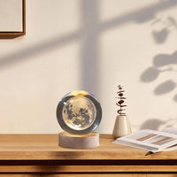 Moon lamp on a wooden surface with a plant and book in the background