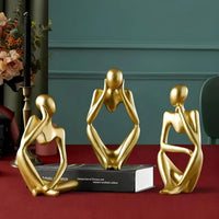 Set of three gold abstract sculptures on a red surface with a teal wall in the background.
