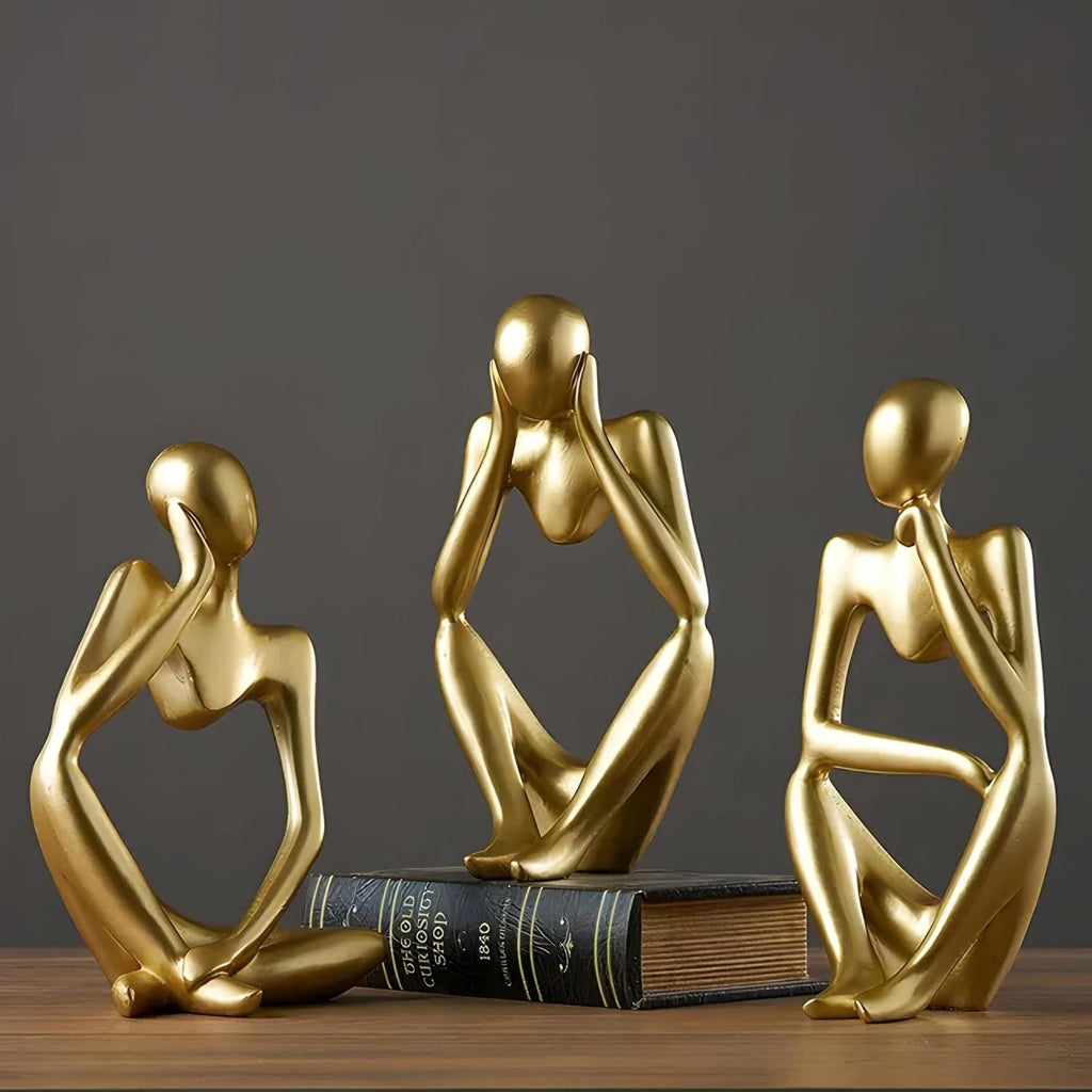 Three gold abstract sculptures on a book against a dark background