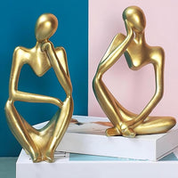 Two gold abstract sculptures on a white surface with a colorful background