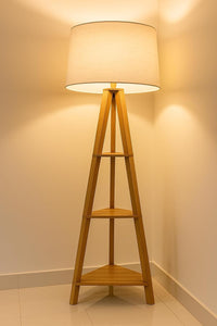 Wooden floor lamp with a white shade against a beige wall.