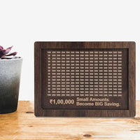 Wooden plaque with monetary values and motivational quote on a wooden surface with a plant.