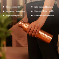 Person holding a copper bottle with health benefits listed on a blurred background